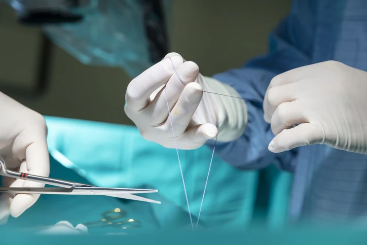 Cirurgião realizando sutura cirúrgica com fio e agulha em ambiente hospitalar