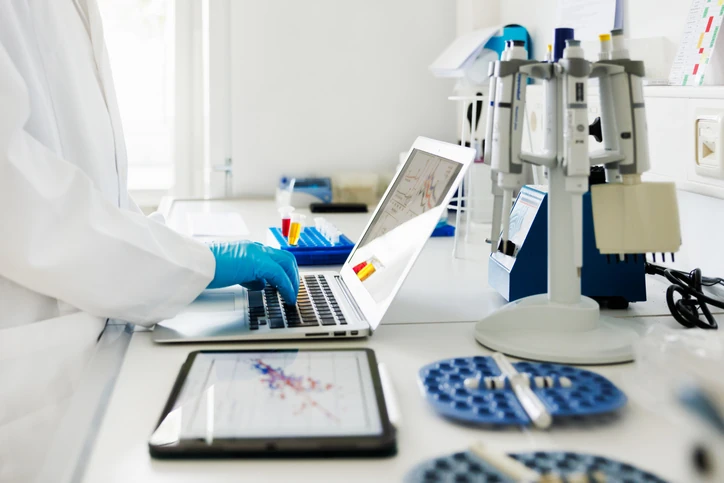 Pesquisador trabalhando em laboratório com laptop e tablet para análise de dados