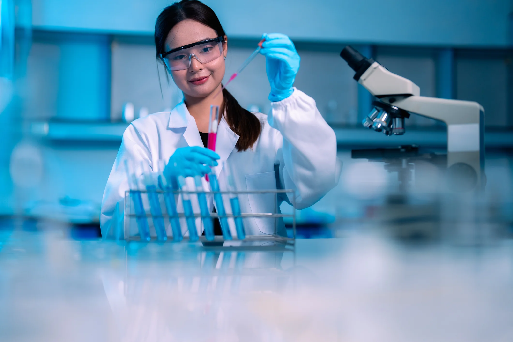 Pesquisadora realizando experimentos em laboratório de biomedicina com tubos de ensaio e microscópio.