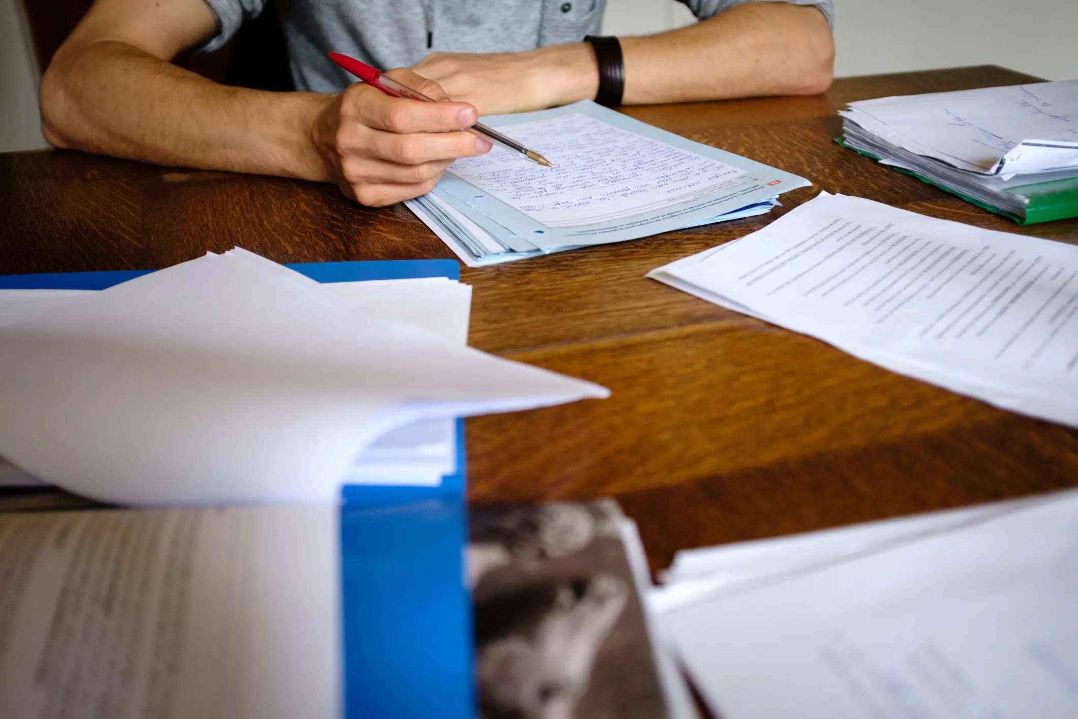 Estudante escrevendo em papel sobre mesa de madeira com materiais de estudo
