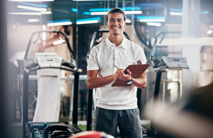 Personal trainer sorrindo segurando uma prancheta em uma academia moderna