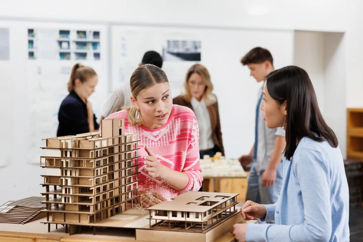 Estudantes de arquitetura trabalham em colaboração analisando uma maquete detalhada de um prédio em um ambiente acadêmico