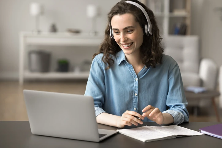 Estudante sorridente utilizando fones de ouvido e notebook para aula online em casa