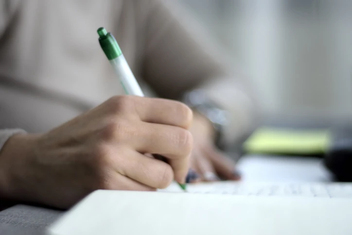 Pessoa focada escrevendo anotações em um caderno para estudos ou planejamento profissional