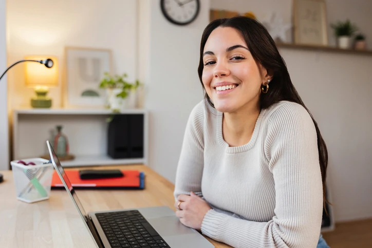 Jovem profissional sorrindo enquanto utiliza um notebook em um ambiente de trabalho remoto organizado e iluminado