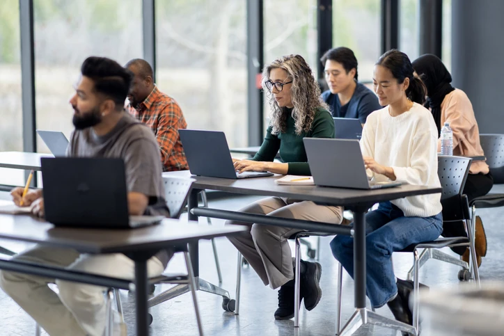 Estudantes universitários focados em seus estudos utilizando laptops em uma sala de aula colaborativa e inclusiva.