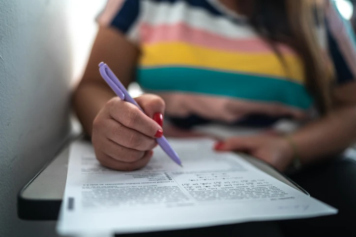 Estudante realizando uma prova escrita com caneta em uma carteira escolar