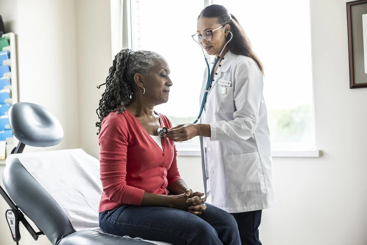 Médica examinando paciente idosa com estetoscópio em consultório