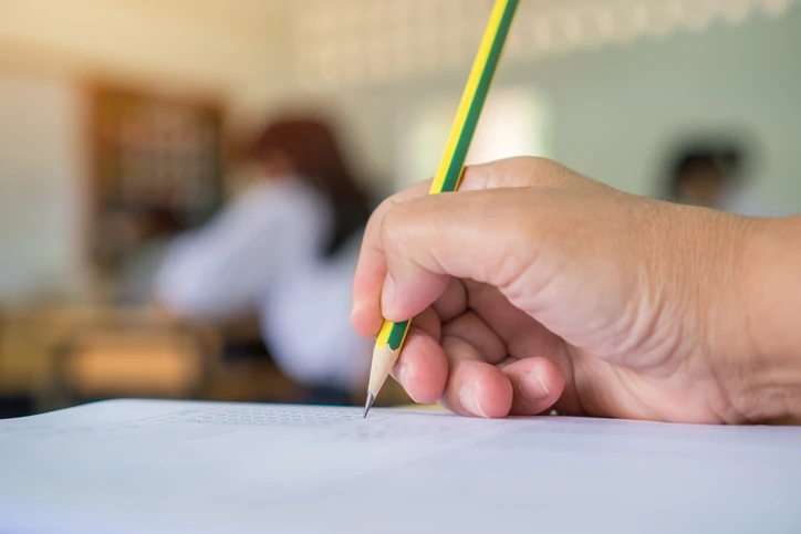 Estudante realizando prova com lápis em folha de gabarito em uma sala de aula
