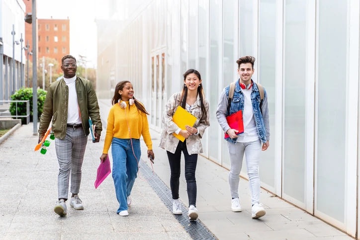 Estudantes universitários diversos caminhando juntos pelo campus da faculdade durante um dia ensolarado