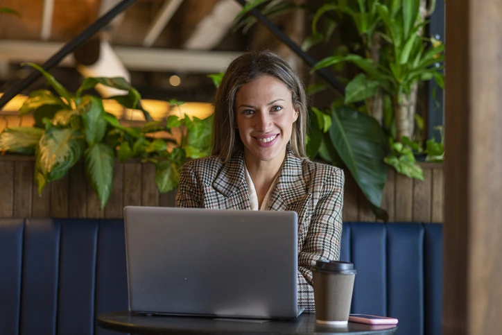 Mulher profissional sorrindo enquanto trabalha em um notebook em um café aconchegante