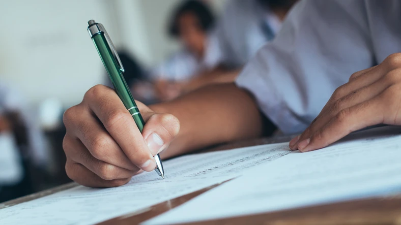 Estudante concentrado respondendo a uma prova escolar com caneta em sala de aula durante exame acadêmico Estudante realizando uma prova em sala de aula com foco na mão segurando a caneta