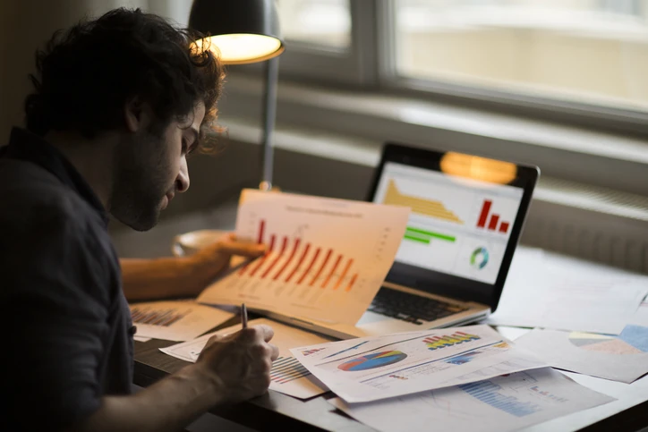 Profissional realizando análise detalhada de dados financeiros e gráficos de desempenho em ambiente de trabalho