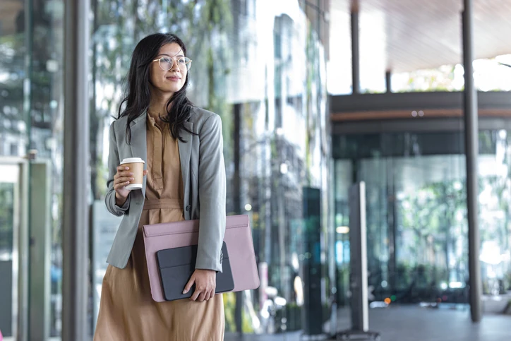 Estudante de administração segurando documentos e café em um ambiente corporativo moderno