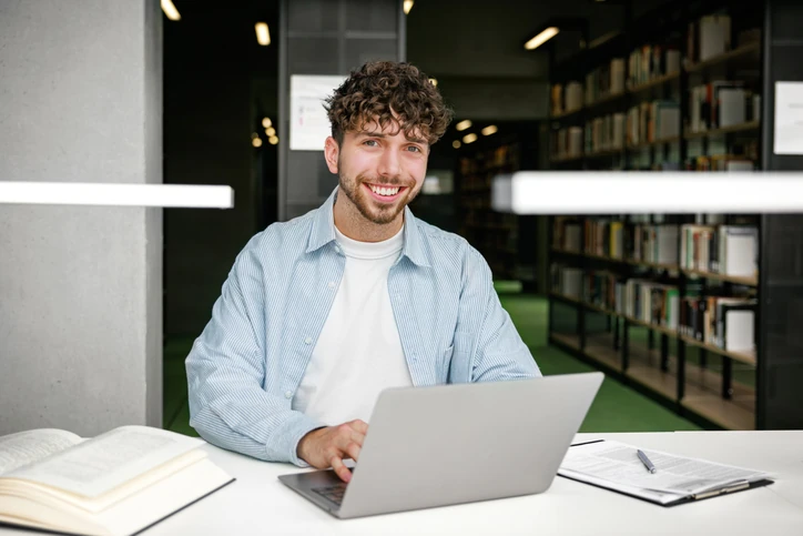 https://estaticos.animaeducacao.com.br/medias/20260126155054/GettyImages-2193883540.webp Estudante universitário focado estudando com notebook e livros em ambiente de biblioteca moderna