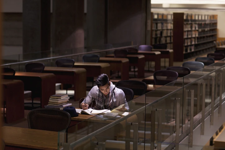 Estudante universitário dedicado estudando em ambiente acadêmico silencioso de biblioteca para melhorar o foco e o aprendizado Estudante focado lendo livros em uma biblioteca silenciosa e organizada