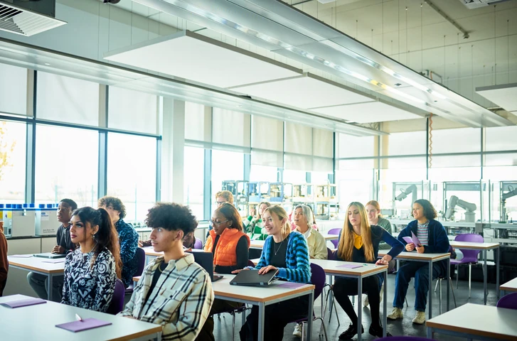 Grupo de estudantes diversos assistindo a uma aula em sala de tecnologia moderna