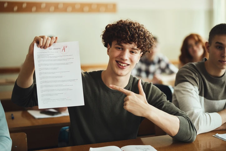 Estudante feliz segurando uma prova com nota A+ em sala de aula