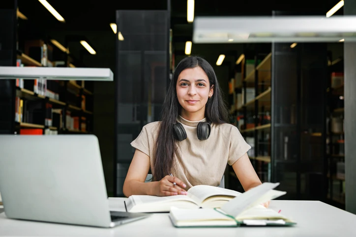 Estudante universitária focada estudando com livros e notebook em uma biblioteca moderna