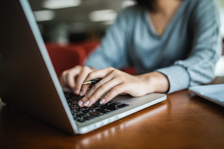Pessoa digitando em um notebook com uma caneta na mão