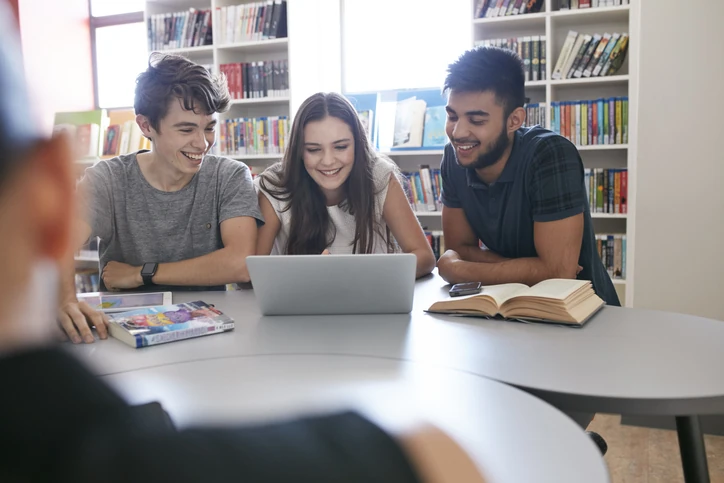 Grupo de estudantes universitários sorridentes estudando juntos com laptop e livros em uma biblioteca