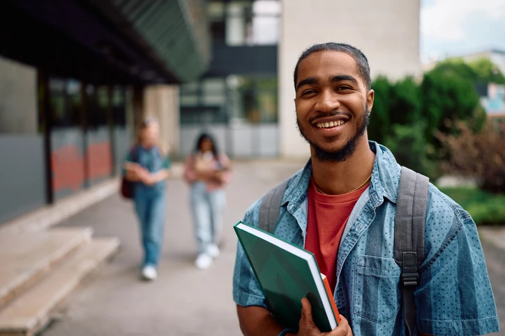 Estudante universitário sorridente segurando cadernos no campus