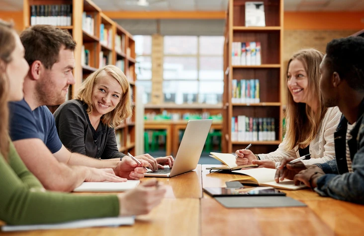 Estudantes universitários trabalhando juntos com notebooks e cadernos em uma biblioteca acadêmica moderna para projetos de pesquisa