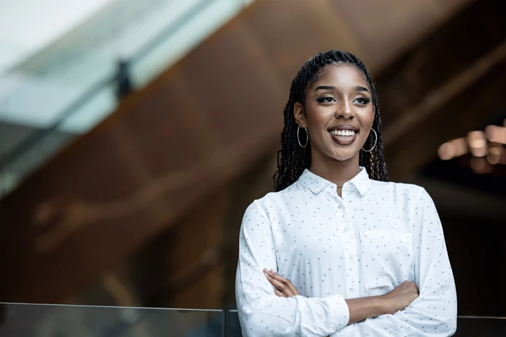Jovem mulher negra profissional sorrindo com braços cruzados em um ambiente corporativo moderno