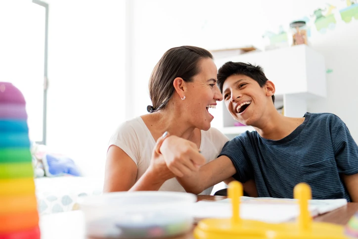 Mãe e filho rindo juntos durante sessão de terapia ou atividade educativa em casa