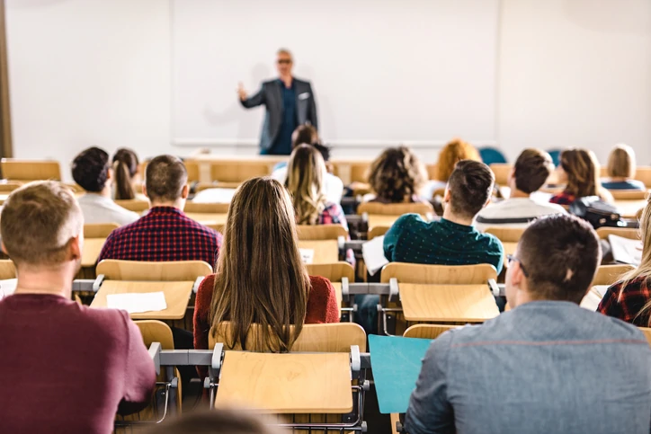 Professor universitário ministrando aula presencial em auditório acadêmico com alunos atentos e engajados no aprendizado