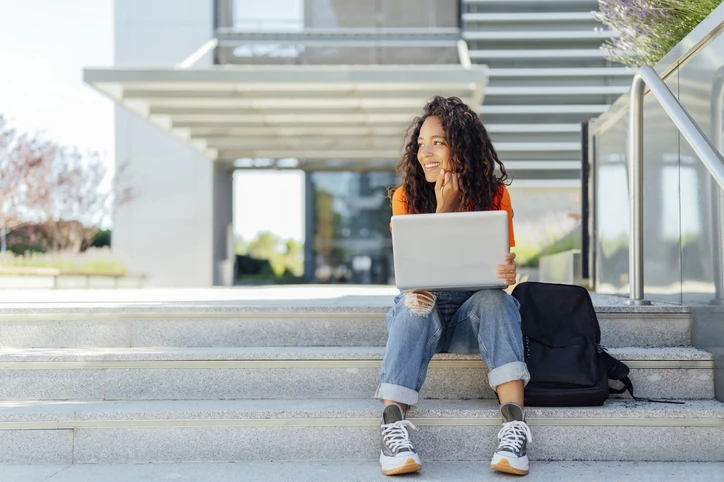 Estudante jovem e feliz realizando pesquisas acadêmicas em seu notebook no ambiente universitário