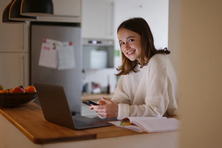 Estudante feliz utilizando tecnologias digitais para realizar tarefas acadêmicas e estudos em casa