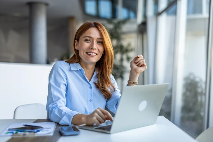 Mulher ruiva profissional sorrindo enquanto trabalha em um laptop no escritório