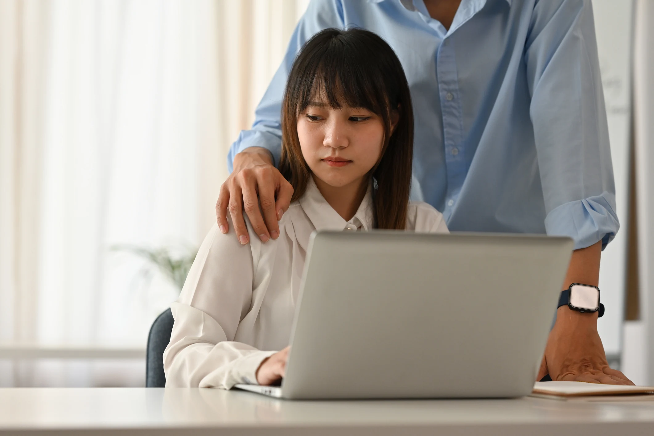 Mulher sentada ao computador com colega ao lado em ambiente de trabalho