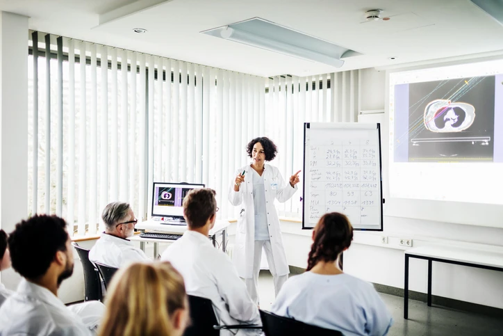 Médica apresentando caso clínico com exames de imagem para equipe de estudantes em treinamento hospitalar