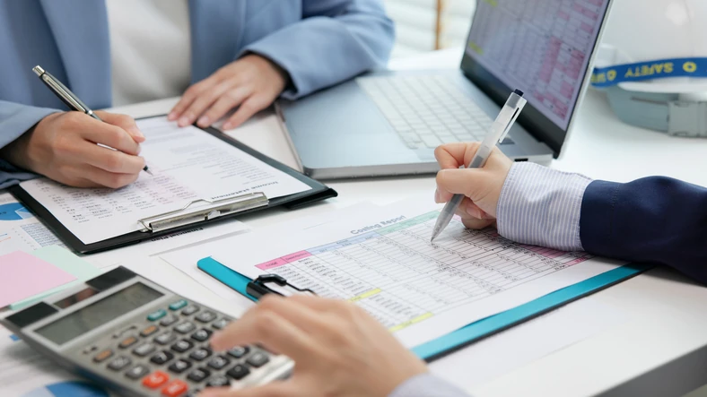 Profissionais analisando relatórios de custos e documentos financeiros em um escritório