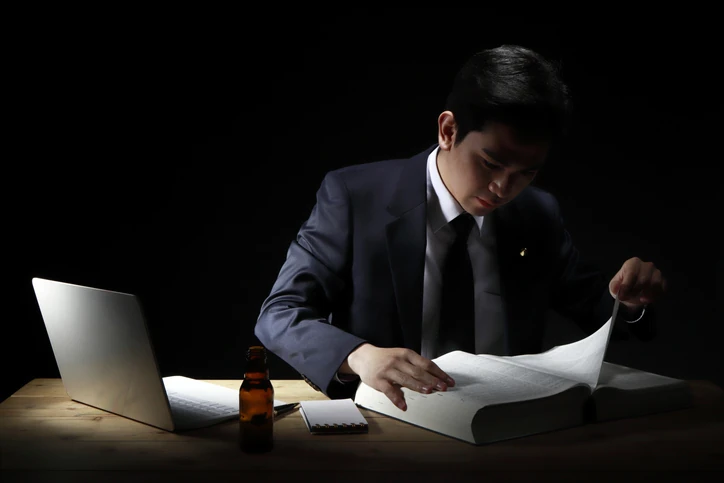 Advogado ou profissional de negócios lendo um livro grande em uma mesa escura com notebook