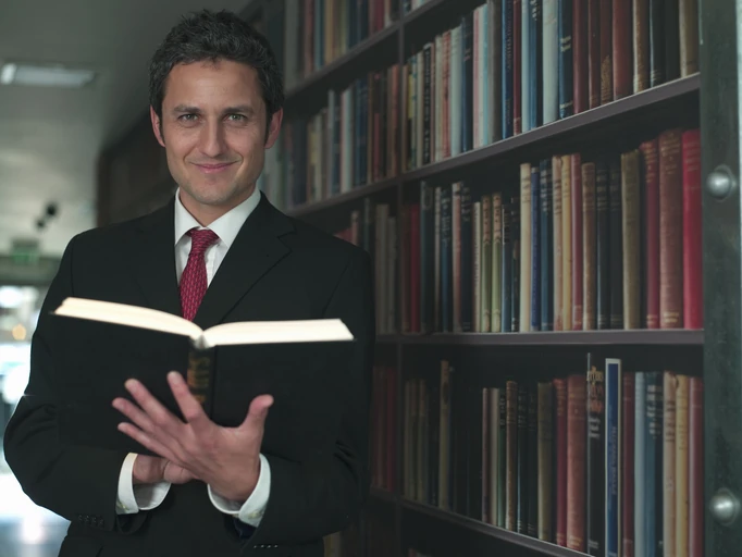 Homem de terno segurando um livro em uma biblioteca