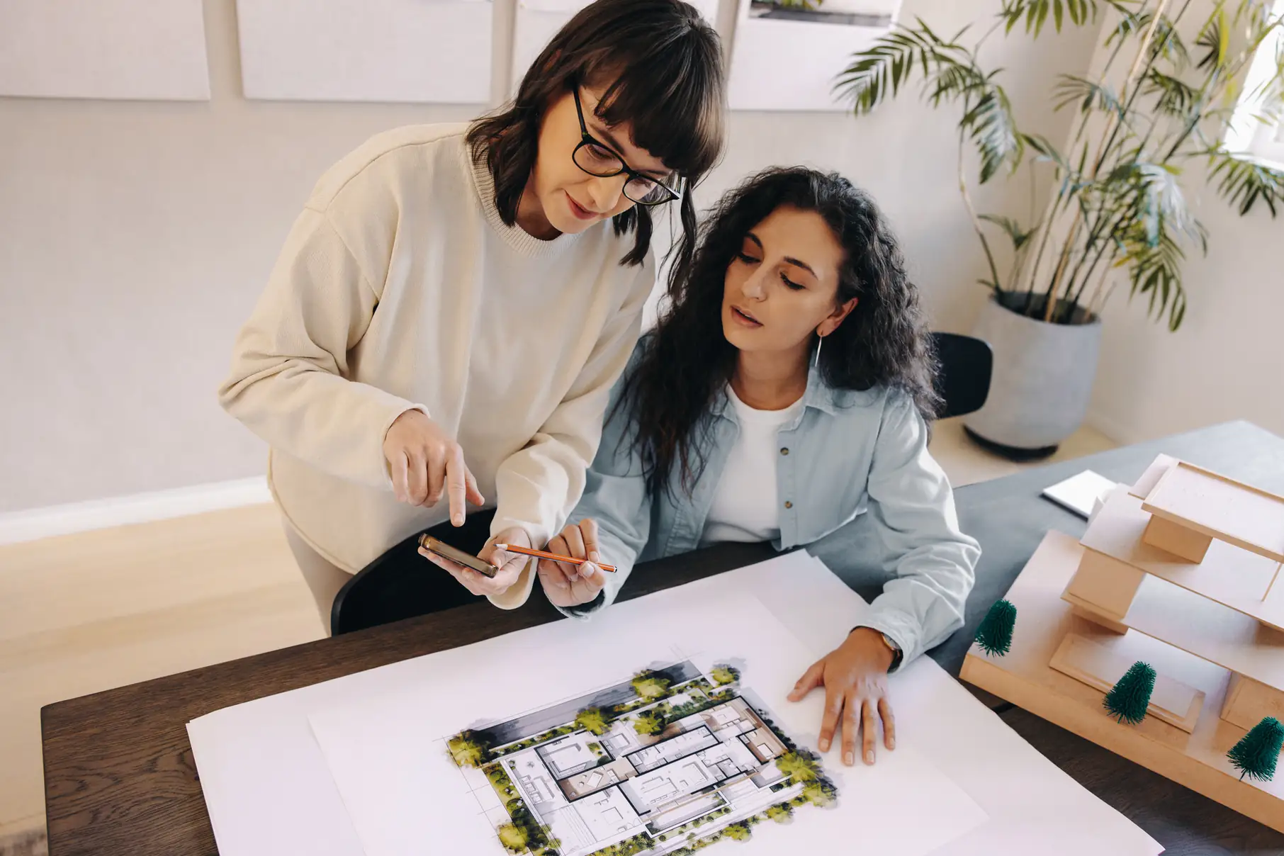 Duas arquitetas trabalhando juntas em um projeto de planta baixa e maquete em um escritório moderno