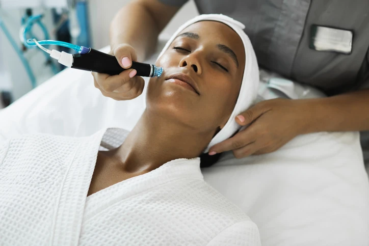 Conheça os benefícios da limpeza de pele profunda e procedimentos estéticos faciais realizados por profissionais qualificados Mulher recebendo tratamento de limpeza de pele com equipamento de microdermoabrasão em clínica de estética