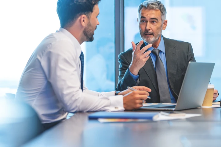 Profissionais de negócios em reunião colaborativa utilizando laptop para análise de dados e estratégia corporativa Dois homens de negócios conversando em uma reunião corporativa com laptop