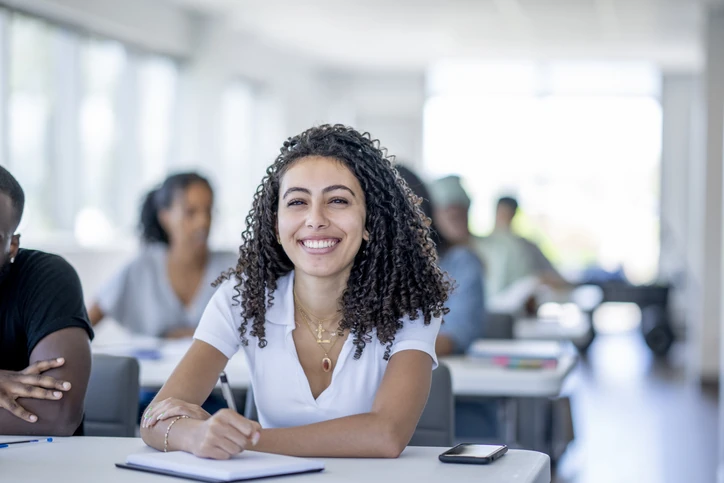 Estudante universitária sorridente participando de aula em sala de estudos com colegas ao fundo