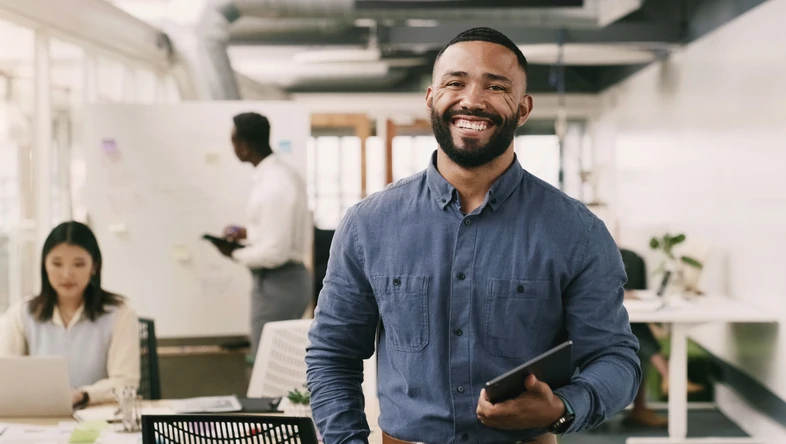 Homem sorridente segurando um tablet em um ambiente de escritório moderno e colaborativo
