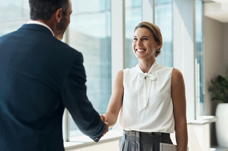 Homem e mulher de negócios sorridentes realizando um aperto de mão em um escritório moderno