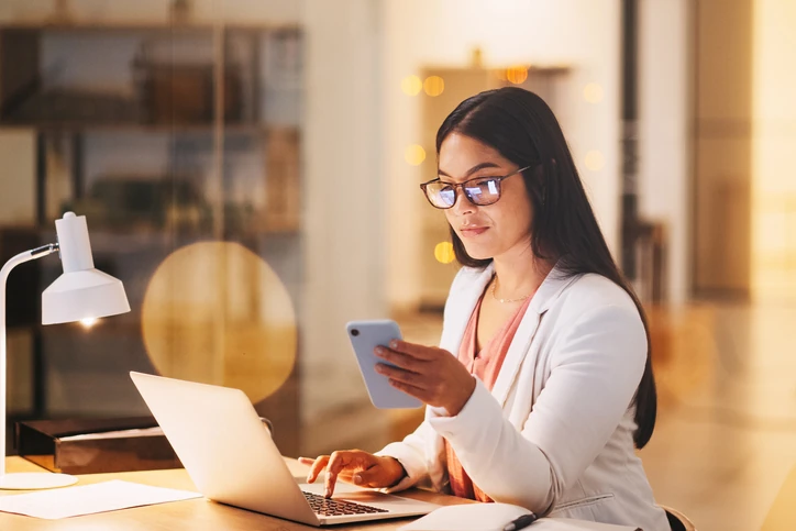 Profissional focada trabalhando no escritório com notebook e celular para produtividade no ambiente corporativo
