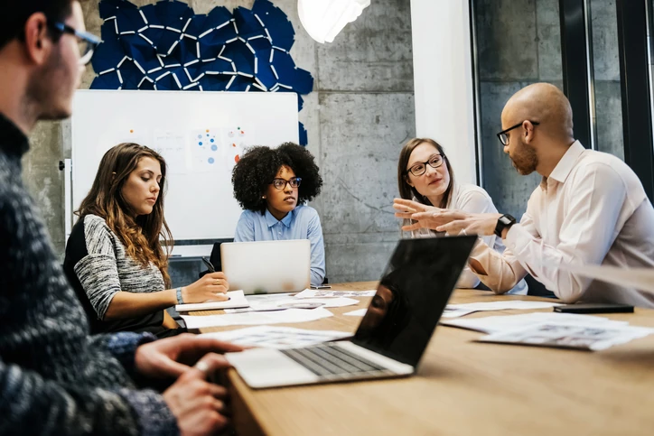 Equipe profissional diversa participando de uma reunião colaborativa de brainstorming em um ambiente de escritório moderno com notebooks e documentos na mesa Equipe diversificada em reunião colaborativa em escritório moderno