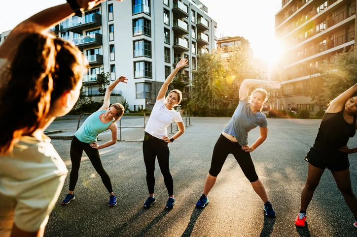 Grupo de mulheres praticando exercícios de alongamento ao ar livre em uma área urbana durante o pôr do sol