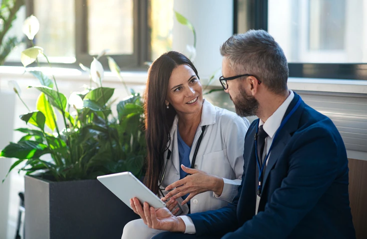 Médica conversando com paciente ou executivo sobre resultados em um tablet dentro de um hospital moderno