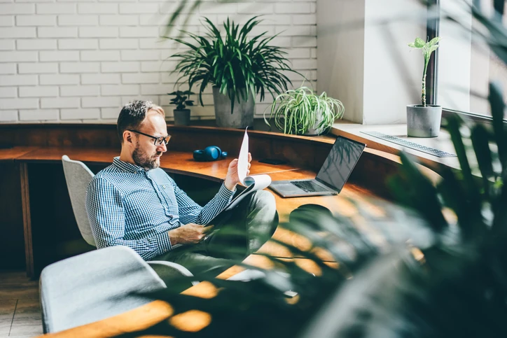 Homem de negócios analisando relatórios em um escritório com plantas e design contemporâneo para um ambiente de trabalho produtivo Profissional de escritório concentrado lendo documentos em um ambiente de trabalho moderno e iluminado