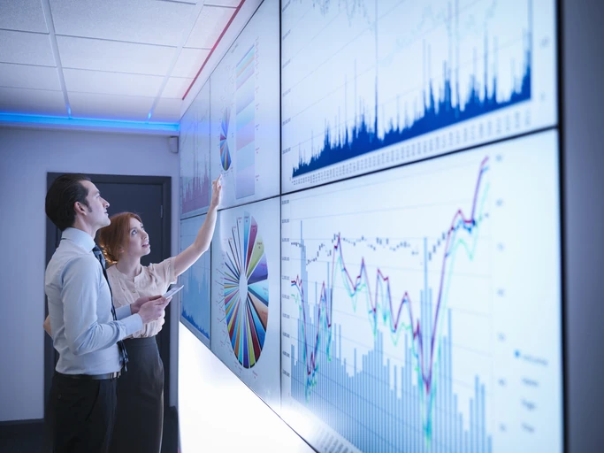 Equipe corporativa analisando gráficos de dados financeiros em uma parede de painéis digitais